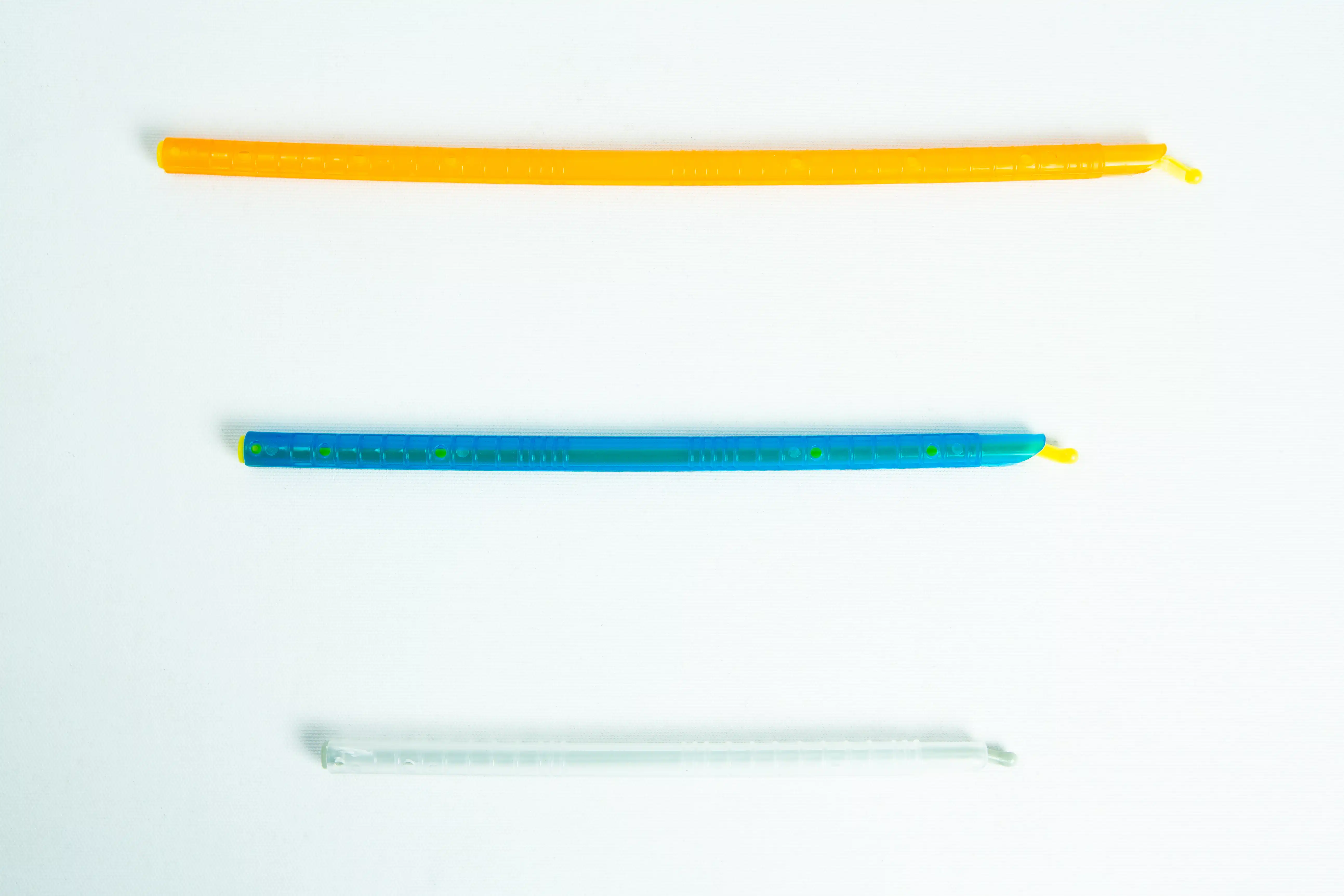 Three colourful twist ties, orange, blue, and clear, are laid out horizontally on a white background.