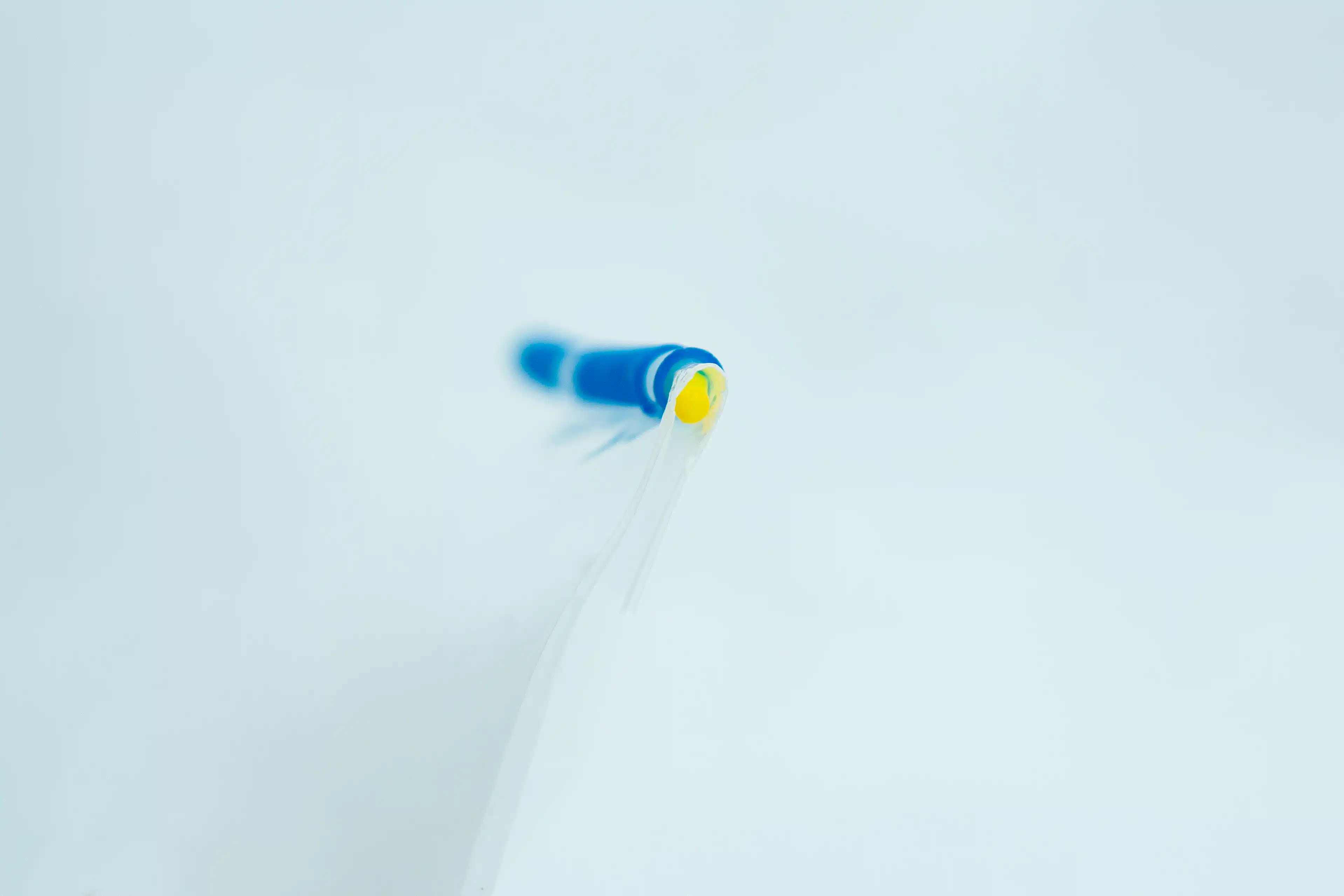 Close-up of a blue and yellow biro tip on a white background, with a shallow depth of field.