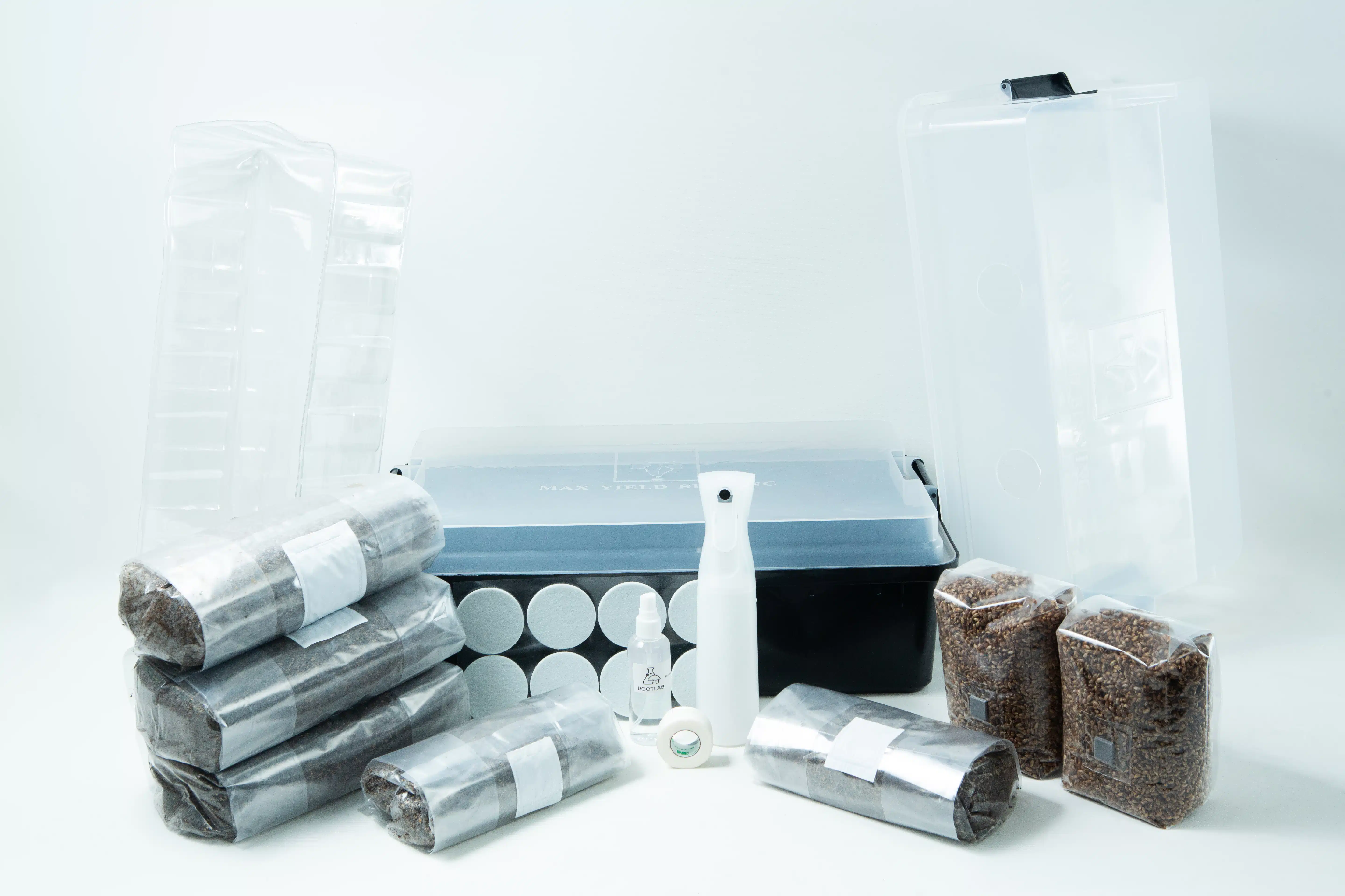 A mushroom growing kit with substrate bags, a clear tub, spray bottle, and accessories on a white background.