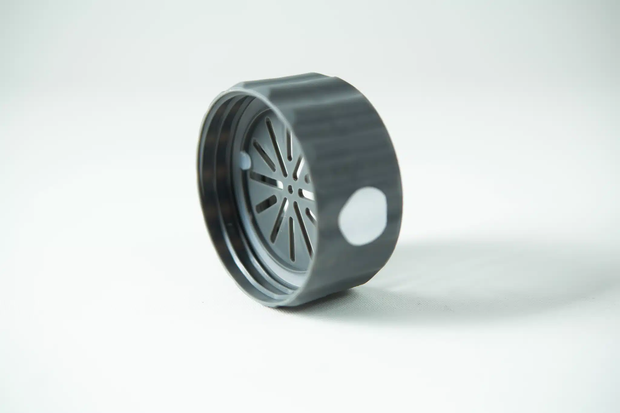 A black plastic circular lid with a slotted inner pattern, from the Plant Cell Biocoupler™ Glass Set (16oz, 12oz, 8oz), is shown on a white surface.