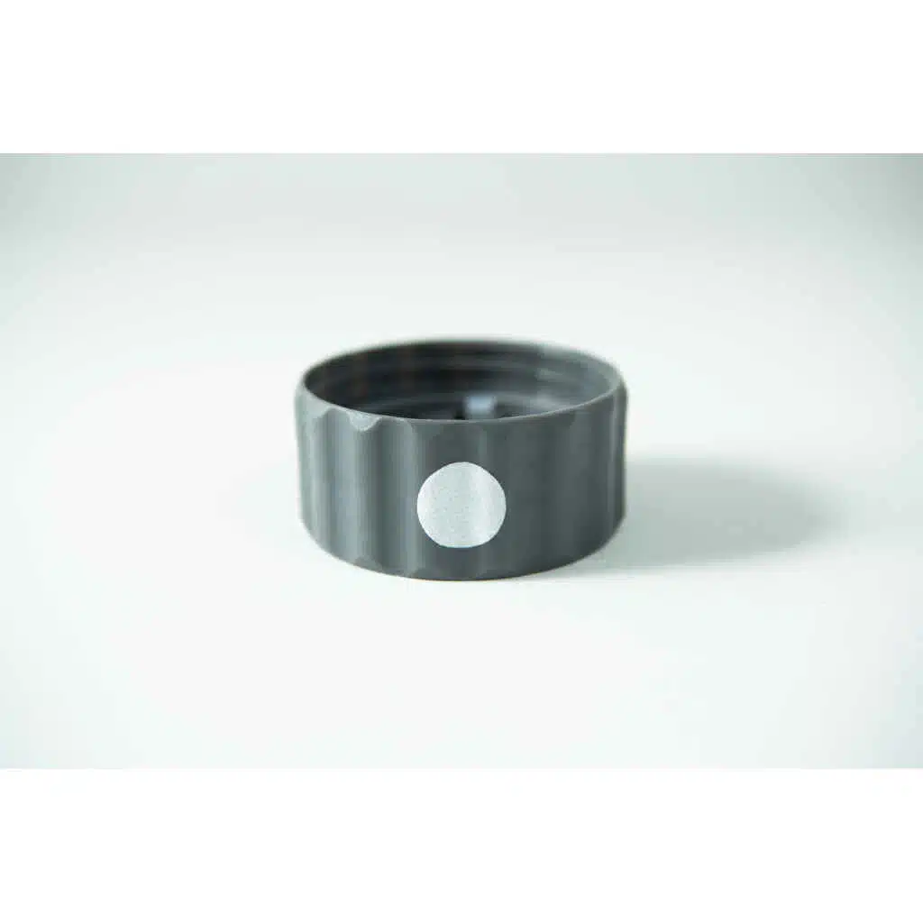 A Plant Cell Biocoupler™ Glass Set bottle cap—grey plastic with a white circular sticker on its side—rests on a white surface.