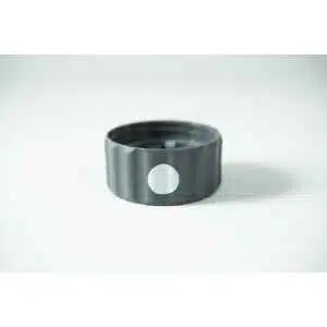 A Plant Cell Biocoupler™ Glass Set bottle cap—grey plastic with a white circular sticker on its side—rests on a white surface.