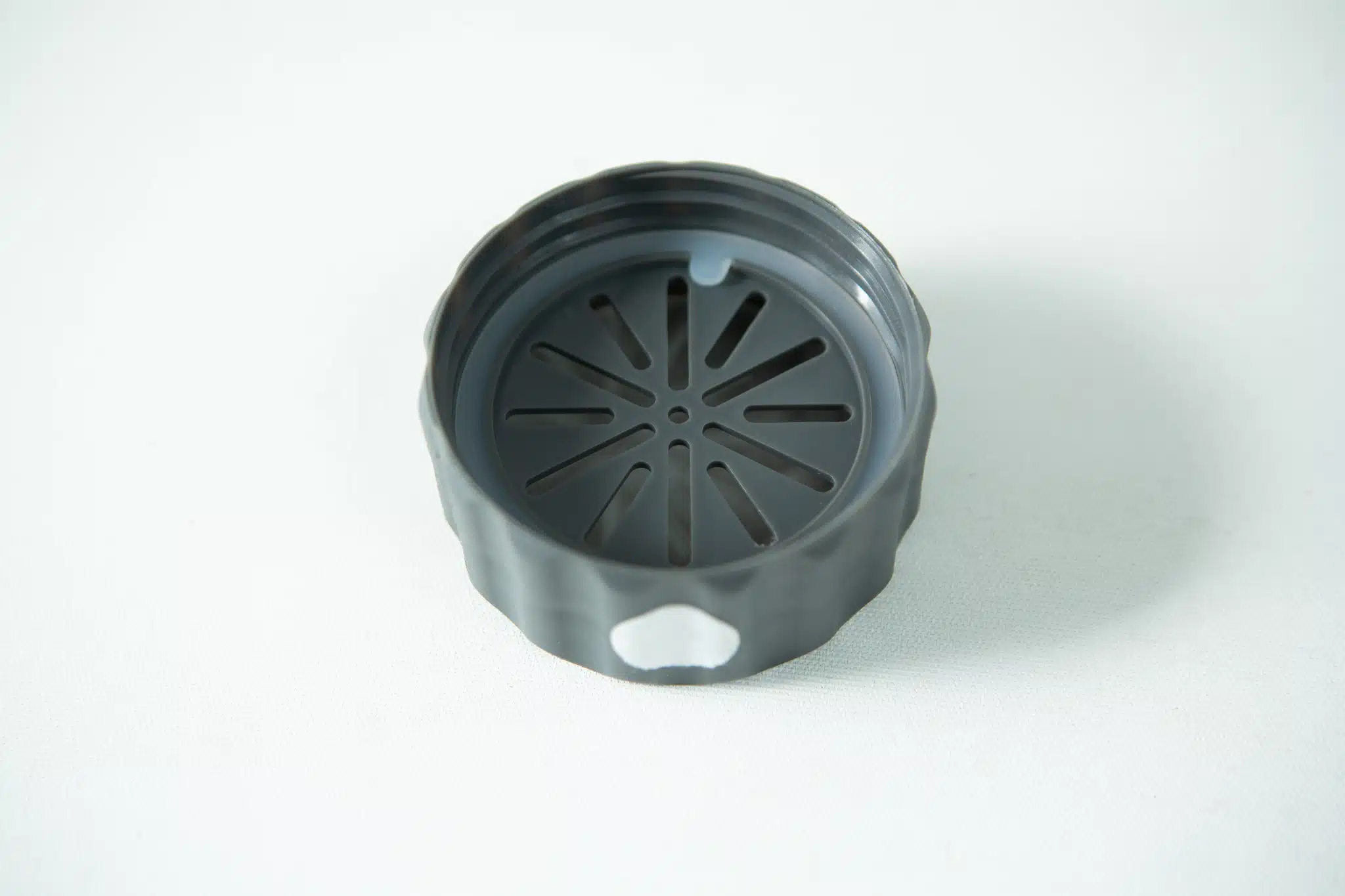 A black, round plastic lid with a slotted vent pattern, designed for the Plant Cell Biocoupler™ Glass Set (16oz, 12oz, 8oz), is shown on a white surface.