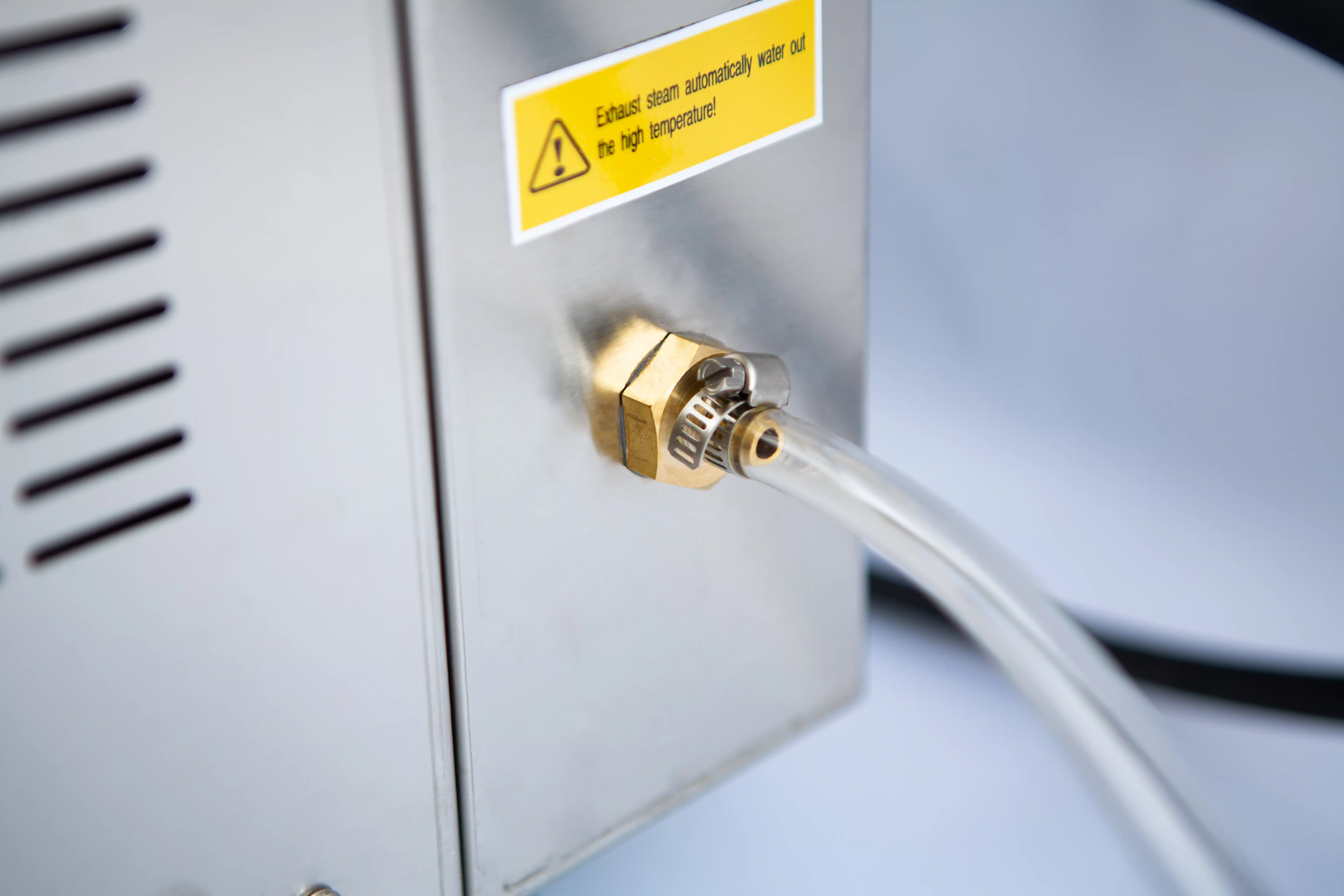 Vertical Autoclave 150 Liters (Automatic) | Commercial use | 6KW 14 Clear tube connected to a brass fitting on a metal machine; warning label about high temperature nearby.