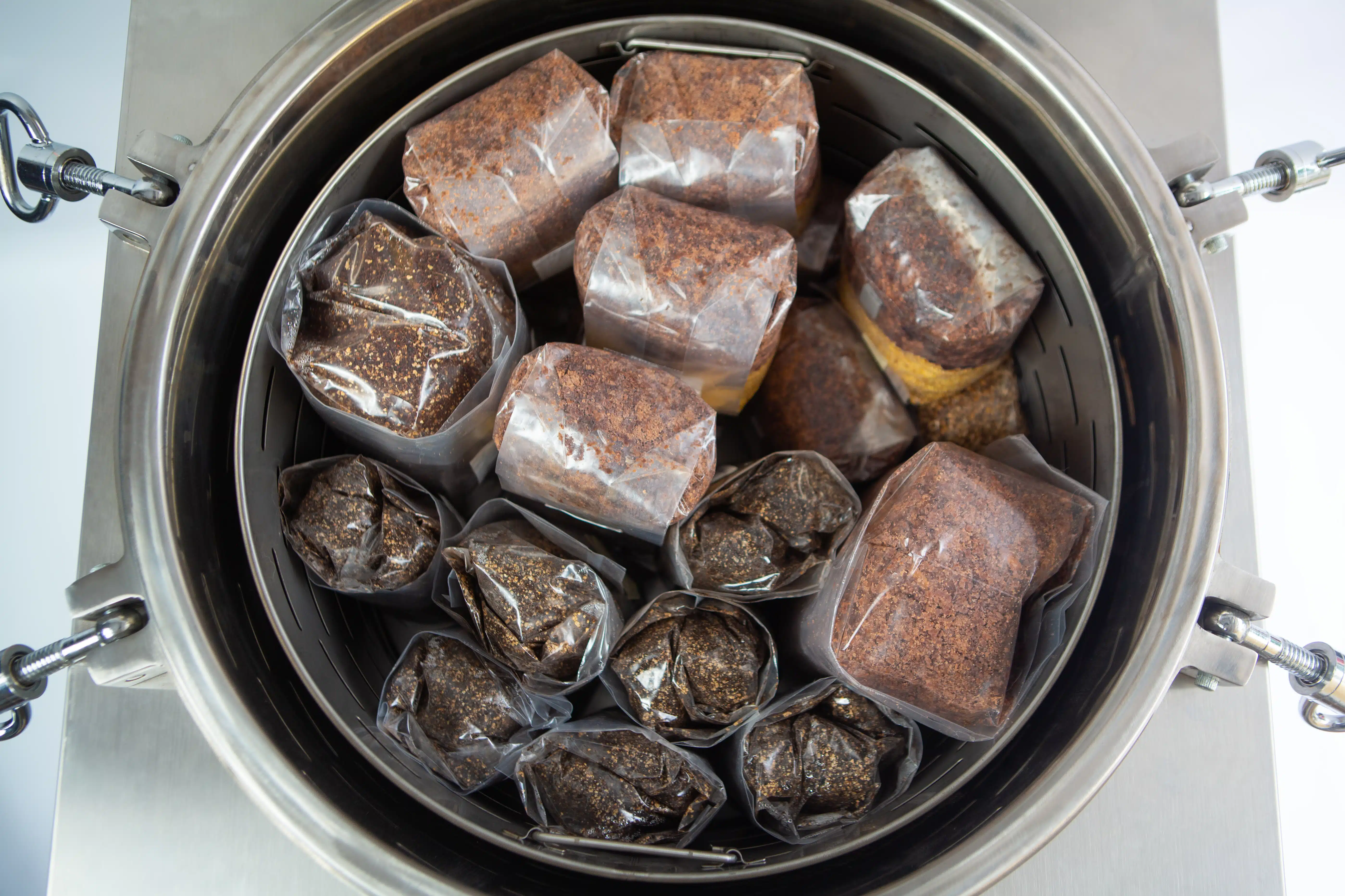 Vertical Autoclave 150 Liters (Automatic) | Commercial use | 6KW 13 Plastic bags filled with a brown substrate inside a metal container, likely for mushroom cultivation.