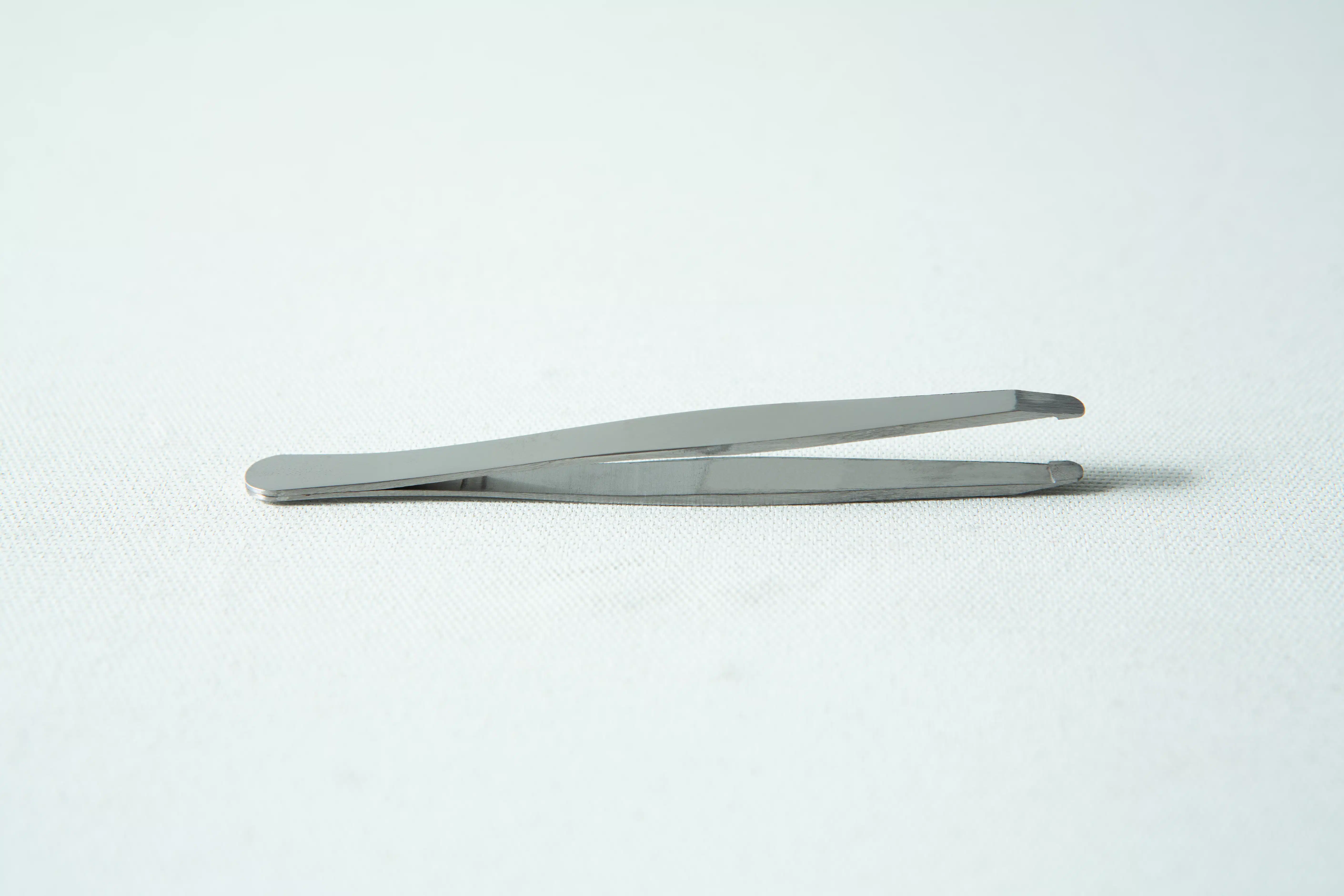 A pair of metal tweezers rests on a white surface, ideal for use with your slime mould kit - Physarum polycephalum.
