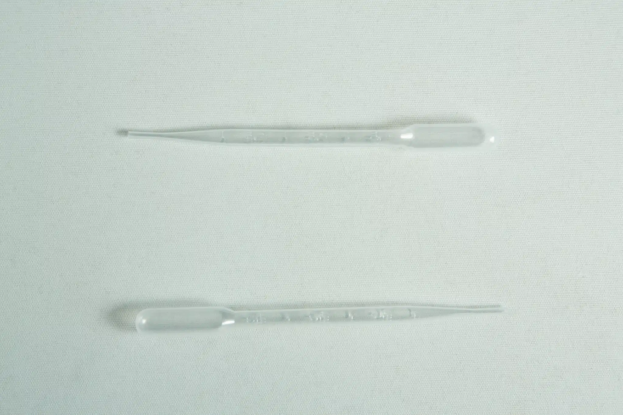 Two clear plastic pipettes from the Plantcell Synthetic Seed Starter Kit lie parallel on a light, textured surface.