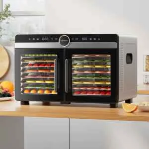 The Devanti 16 Trays Food Dehydrator Dual-Zone Stainless Steel, filled with trays of sliced fruit and vegetables, sits on a kitchen worktop.