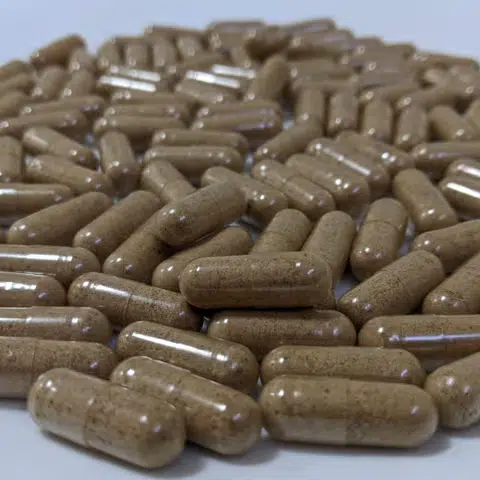 A pile of brown Australian Lion’s Mane herbal supplement capsules scattered on a white surface.