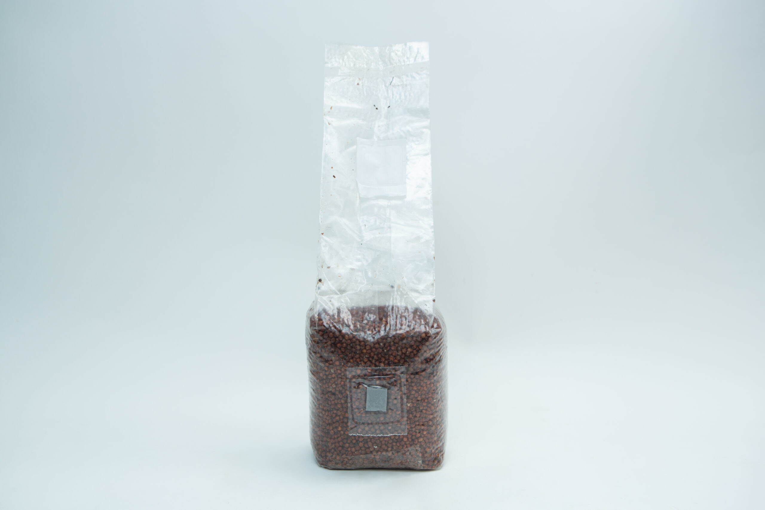Sorghum(Milo) Pre sterilised for mushroom cultivation w/inj port and air-filter 1kg 2 A sealed, clear plastic bag filled with small brown beans, standing upright against a white background.