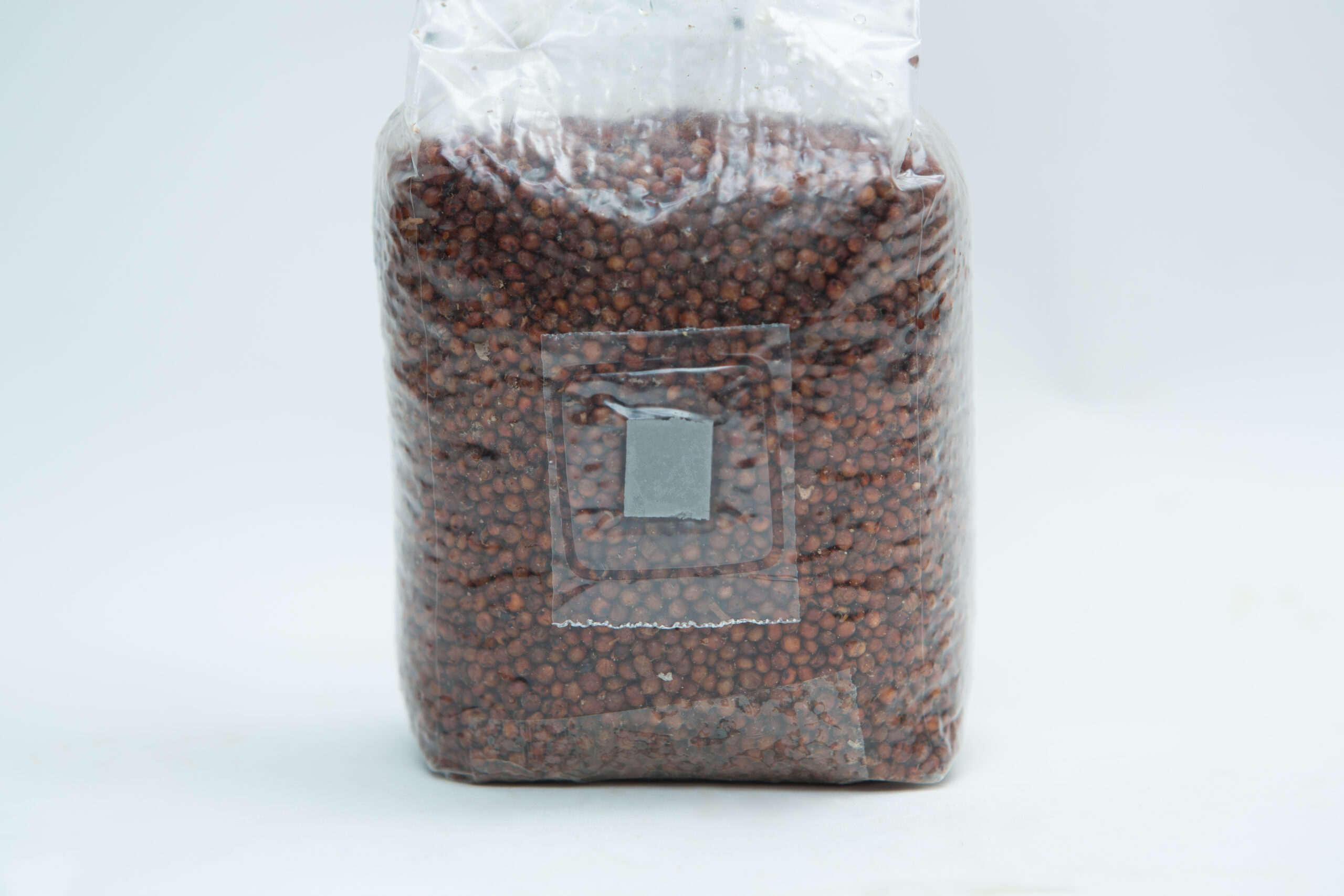 Sorghum(Milo) Pre sterilised for mushroom cultivation w/inj port and air-filter 1kg 1 A sealed plastic bag filled with small brown seeds or grains on a plain white background.