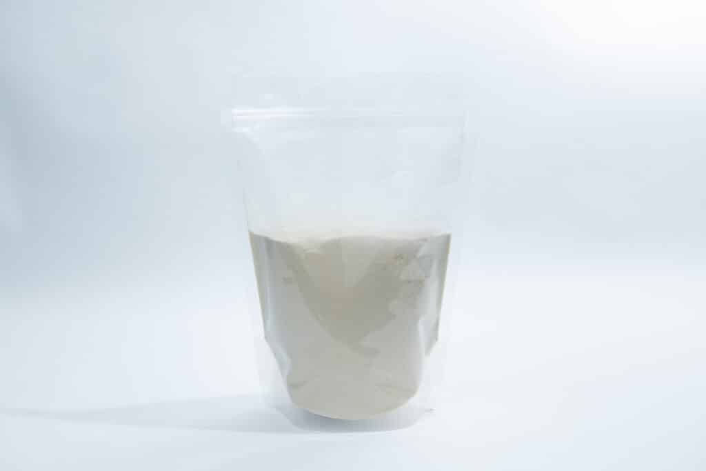 A clear resealable bag filled halfway with a light beige powder, set against a white background.