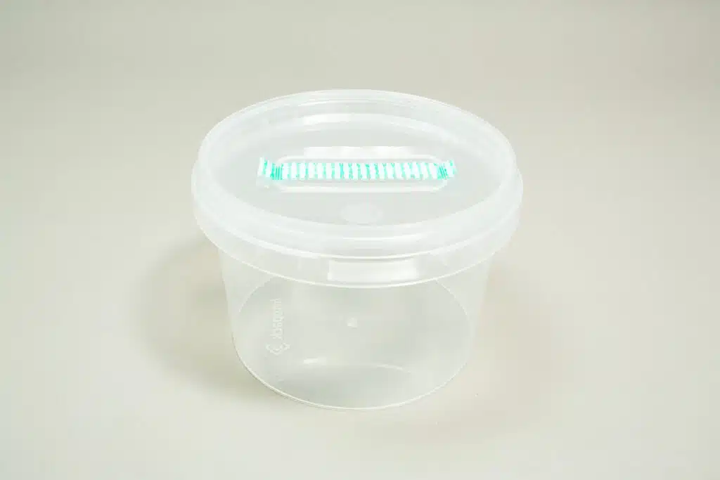 Clear plastic container with a round lid and a rectangular vent or window on top, placed on a plain surface.