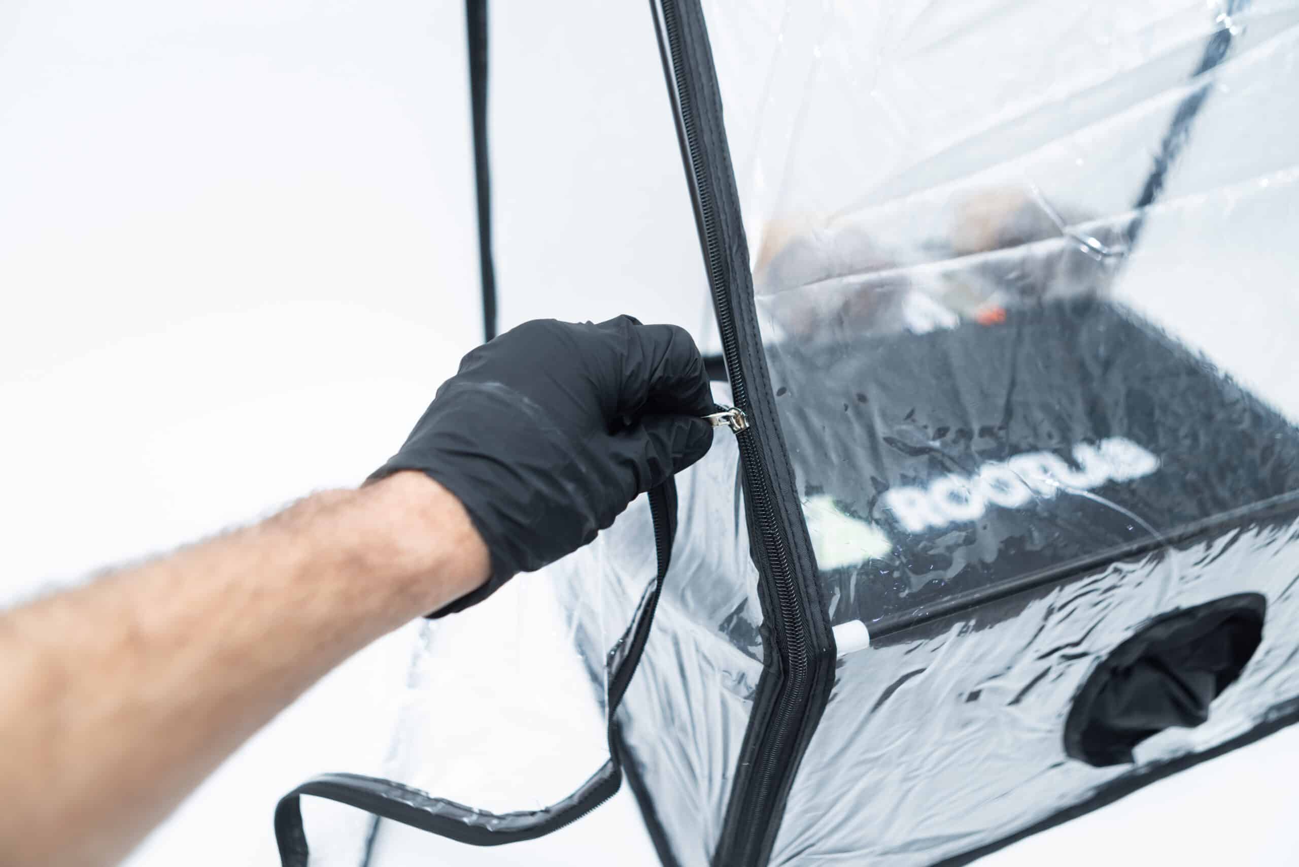 Rootlab Still Air Box with viewing Window Angled 4 A gloved hand unzips the clear Rootlab Still Air Box with Viewing Window Angled, revealing the setup inside through the convenient viewing window with Rootlab branding visible.
