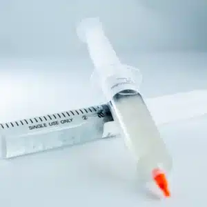 Two syringes with orange caps, one filled with clear liquid and the other with white liquid, on a white surface.