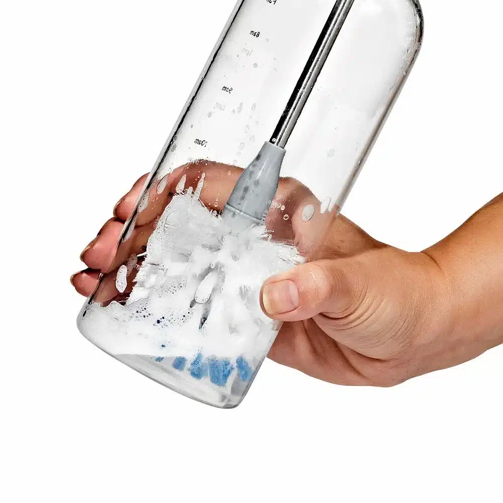 OXO Good Grip Stainless Steel Bottle Brush with replaceable head 4 A hand cleaning a clear bottle with a brush and soapy water inside.